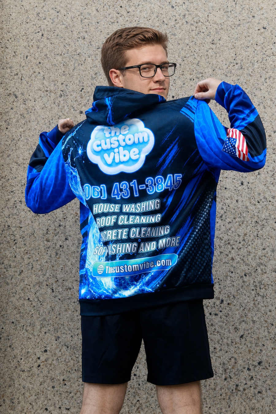 Man wearing a custom all-over-print The Custom Vibe hoodie showing the pressure washing company logo, phone number, services and website printed on the back